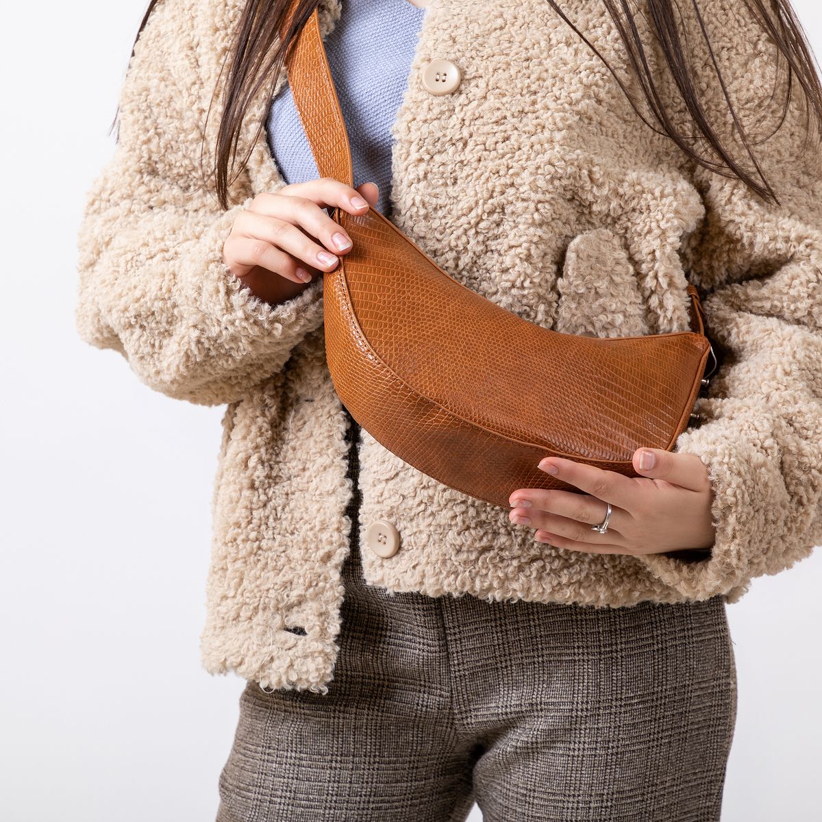 A woman carrying a brown crossbody bag with a refined neutral outfit