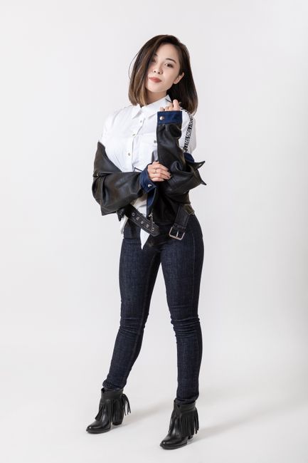 Asian woman posing with confidence in black leather jacket and jeans against a white background.