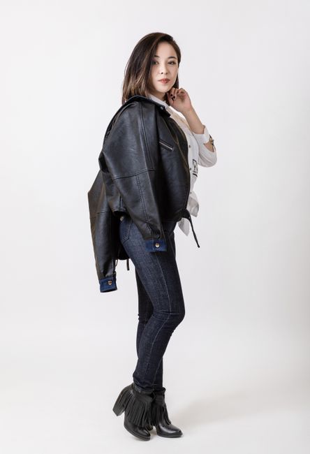 Stylish woman posing in a leather jacket and jeans against a white background.