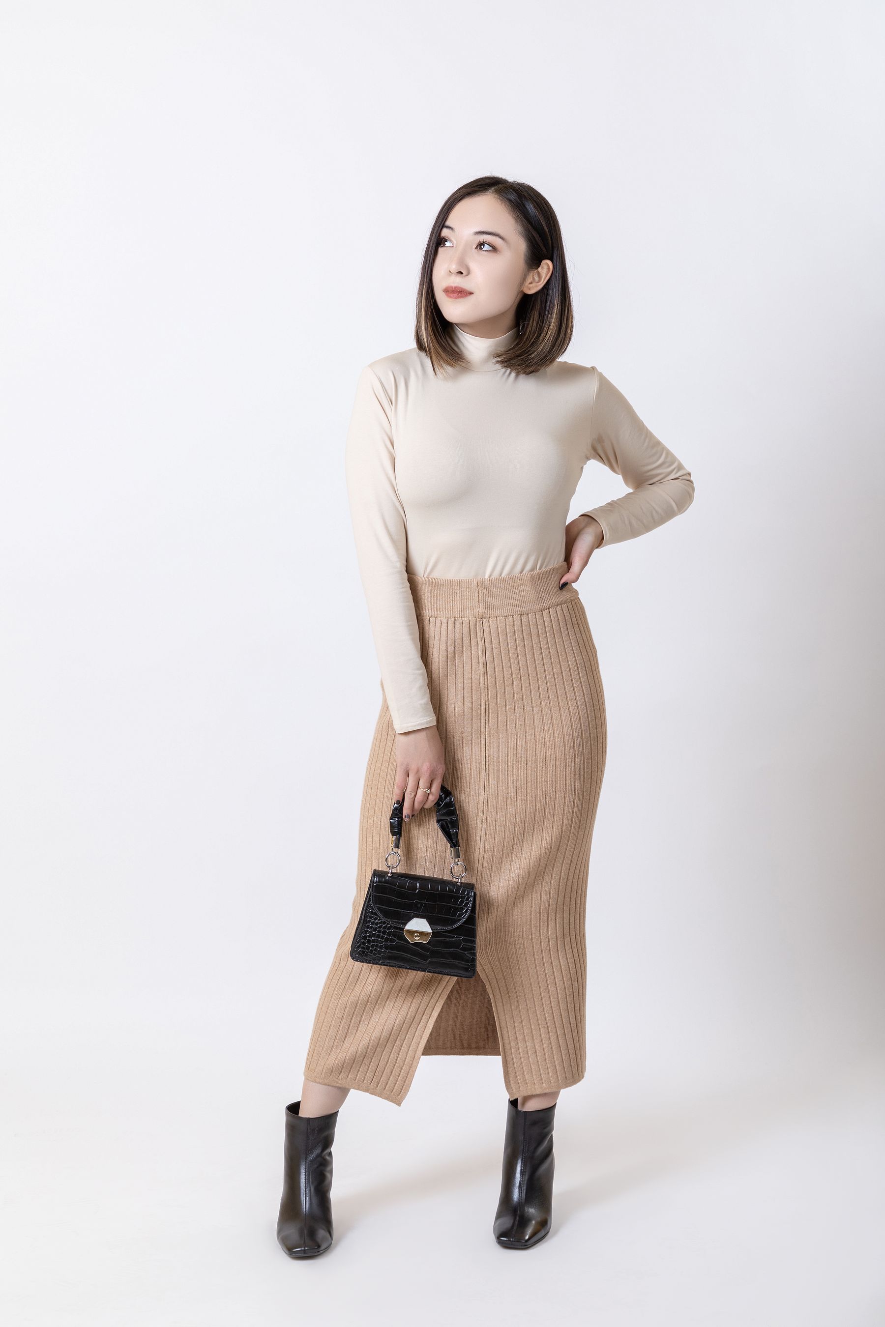 Woman in a refined beige outfit holding a structured black handbag in a bright studio