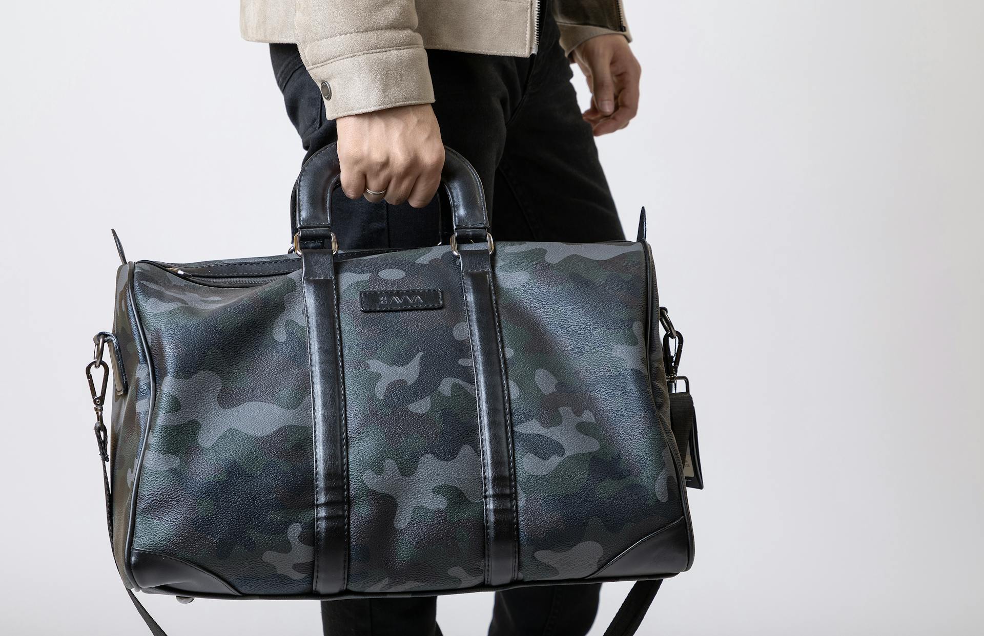 Close-up of a man holding a trendy camouflage leather travel bag in a studio setting.