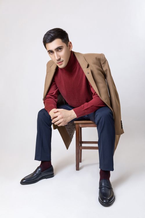 Free Portrait of an elegant man in a stylish coat sitting in a studio setting. Stock Photo