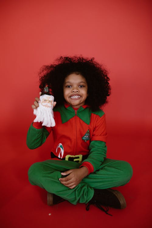 Child in an Elf Costume holding a Santa Claus Ornament 