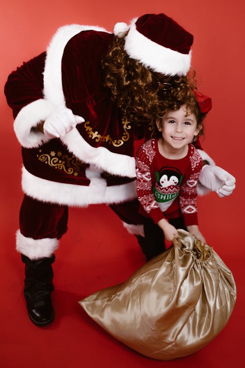 Person in Santa Claus Costume Standing Beside a Girl Holding a Sack