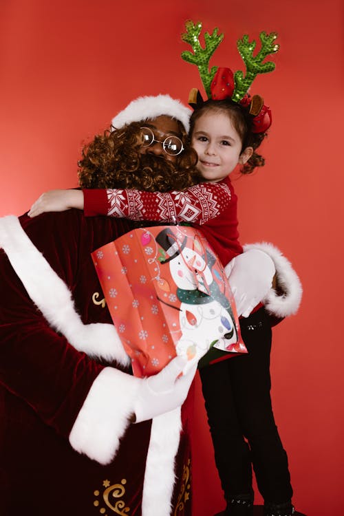 A Girl Hugging a Man Wearing Santa Claus Costume Holding a Paper Bag