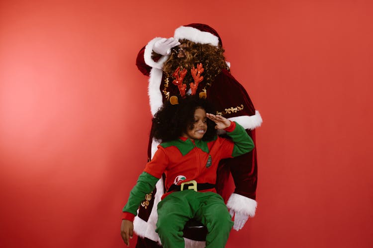 A Man In Santa Claus Suit And A Kid Wearing Elf Costume Saluting