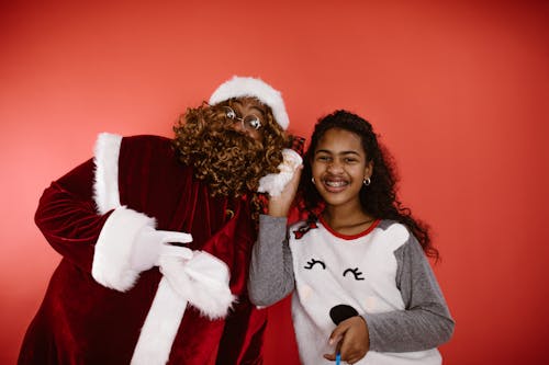 A Man in Santa Claus Costume Beside a Girl in Pajama Holding a Santa Claus Toy