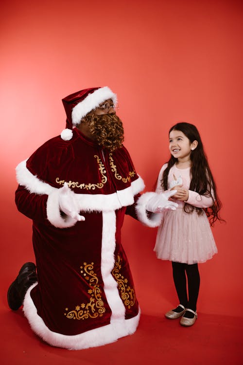 A Man in Santa Claus Costume Kneeling Beside a Girl