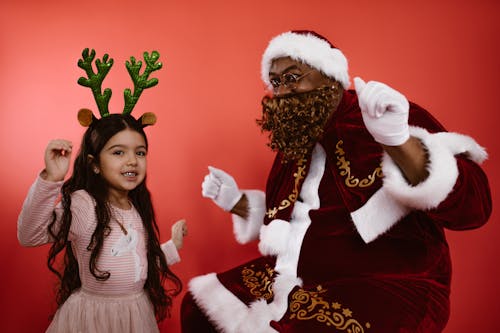 Happy Girl in Pink Dress Standing Beside a Man in Santa Claus Costume