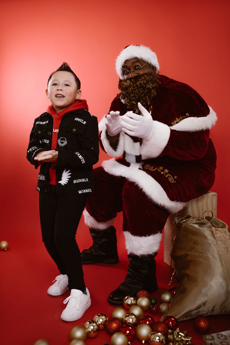 A Boy In Black Hoodie And A Man In Santa Claus Costume Singing Together