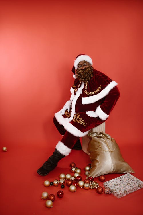 A Man in Santa Claus Costume Sitting on a Wooden Platform while Looking at the Camera