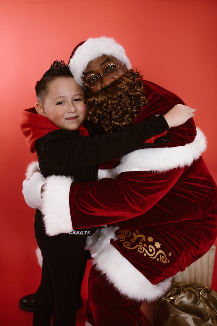 A Boy In Black Hoodie Hugging A Man In Santa Claus Costume