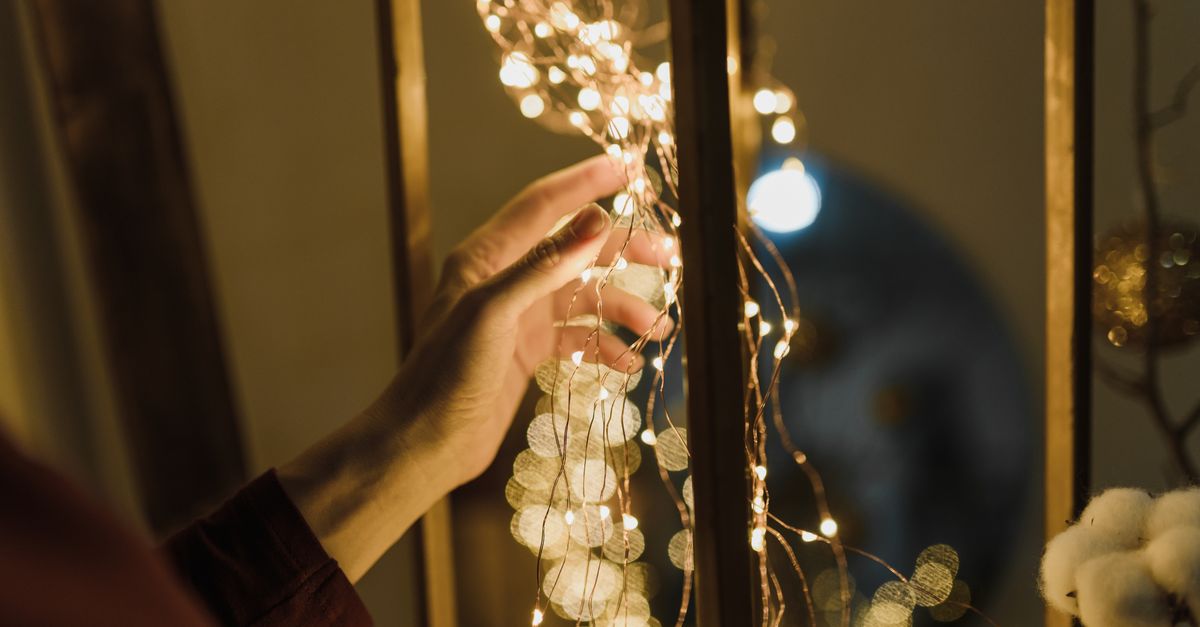A warm indoor scene featuring a hand delicately holding glowing fairy lights, evoking a festive mood.
