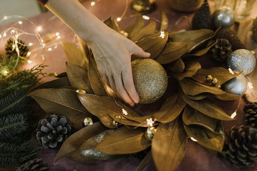 A Person Holding a Gold Christmas Bauble on Top of Gold Dried Nest of Leaves