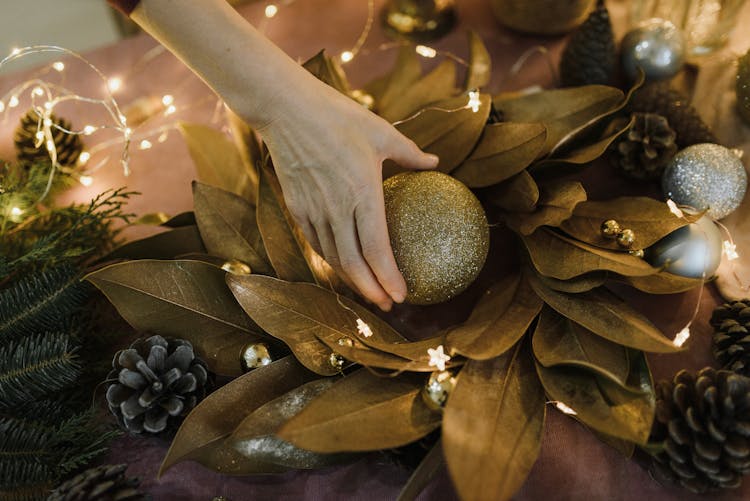 A Person Holding A Gold Christmas Bauble On Top Of Gold Dried Nest Of Leaves