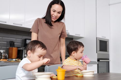 Free Smiling mother watching her two young sons enjoy a healthy breakfast in the kitchen. Stock Photo