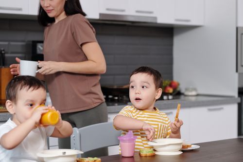 Free Two young boys enjoying their breakfast in a modern kitchen setting with their mother nearby. Stock Photo