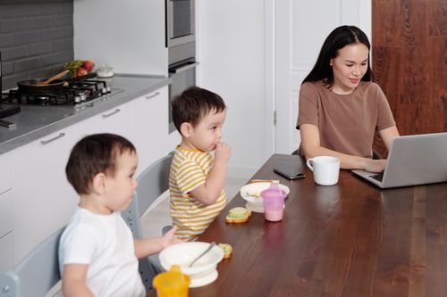 Free A mother multitasking with her children and laptop during breakfast at home. Stock Photo