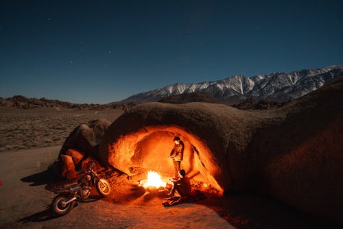 бесплатная Человек в черной куртке сидит на коричневом песке в ночное время Стоковое фото