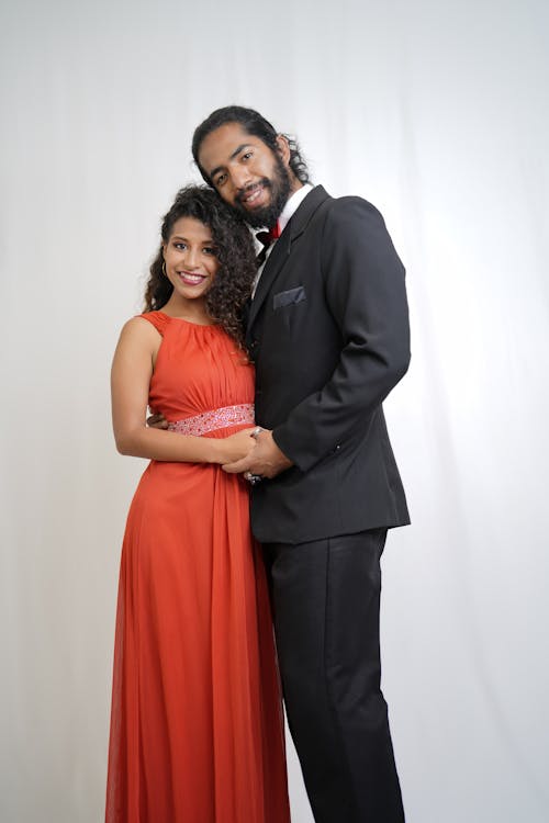 A Man in Black Suit Embracing a Woman in Orange Dress