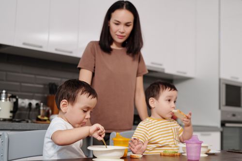 Free A mother watches her children enjoying breakfast in a modern kitchen setting. Stock Photo