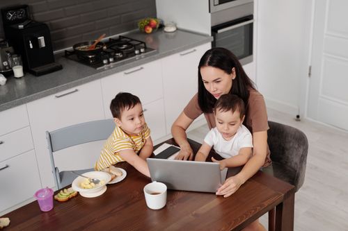 Free A mother multitasks on her laptop with her two young sons in a modern kitchen setting. Stock Photo