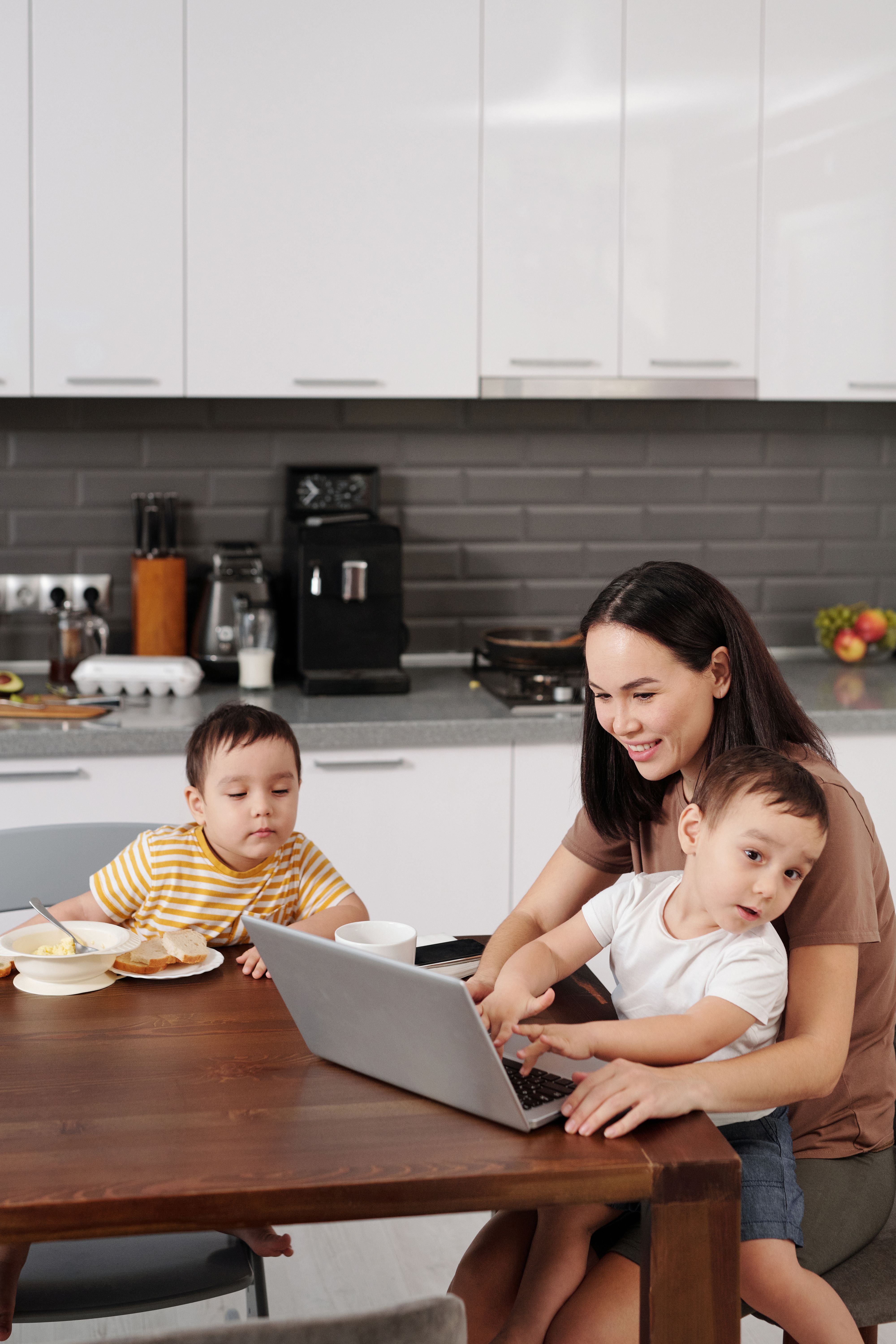 A mother with her two sons interacting with a laptop in a modern kitchen setting.