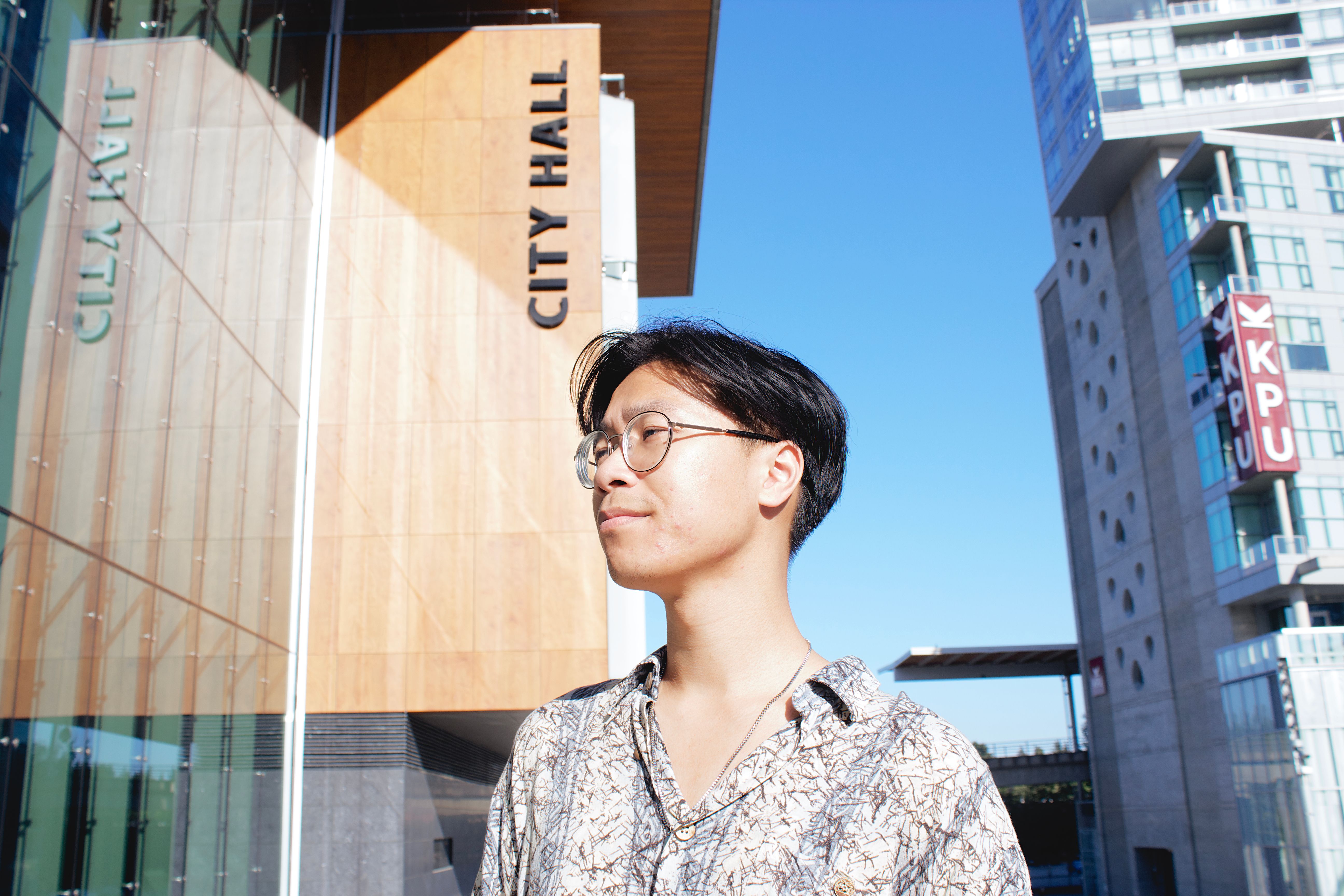 Side profile of a man wearing eyeglasses in front of a modern City Hall building.