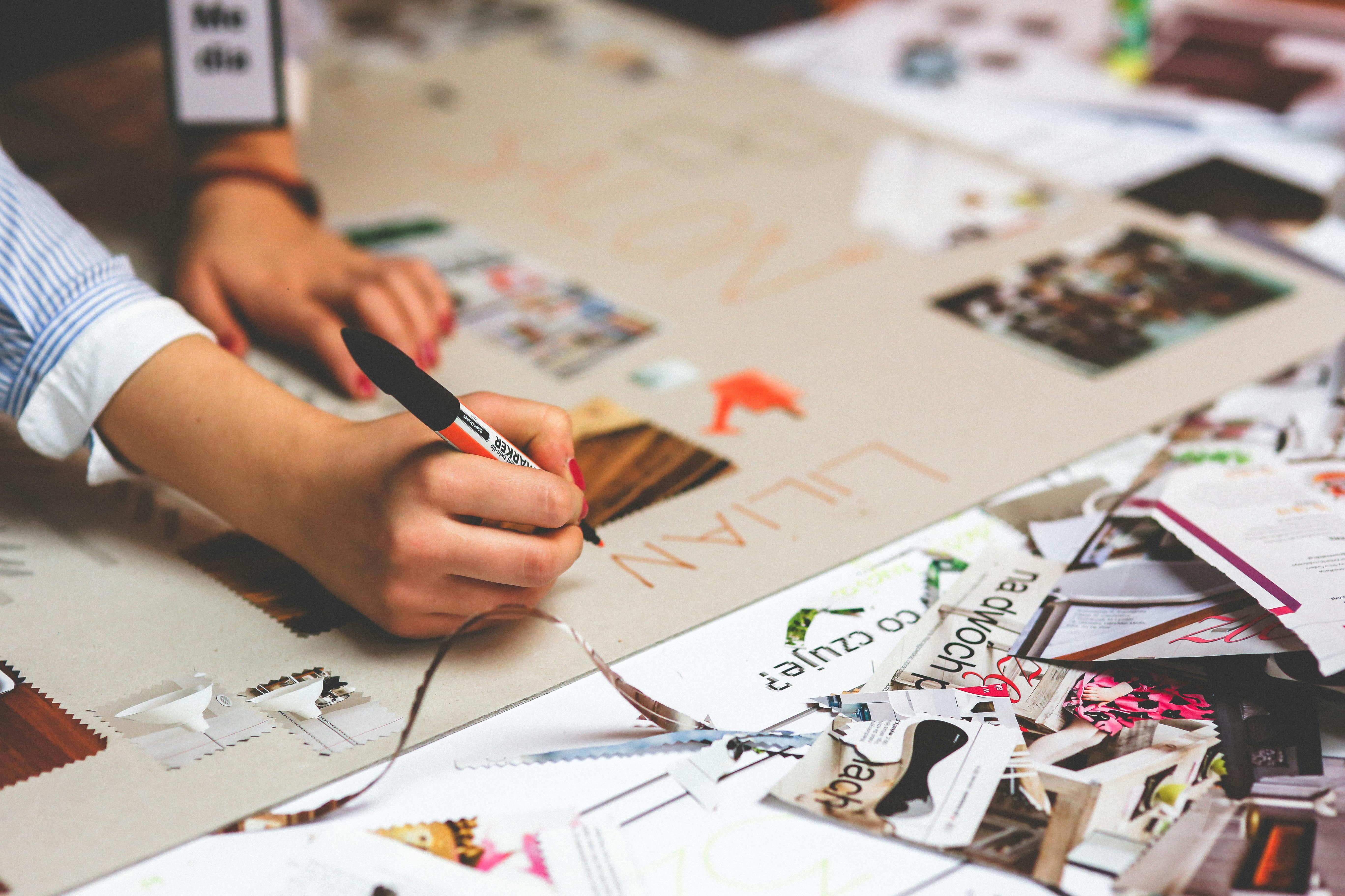 Woman making a vision board with stationary like newspapers, pens and cardboard