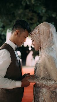Asian couple in traditional wedding attire holding hands with warm expressions. - Fotografer Sidoarjo