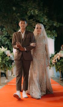 A beautifully dressed bride and groom walking down the aisle during a wedding ceremony. - Fotografer Sidoarjo