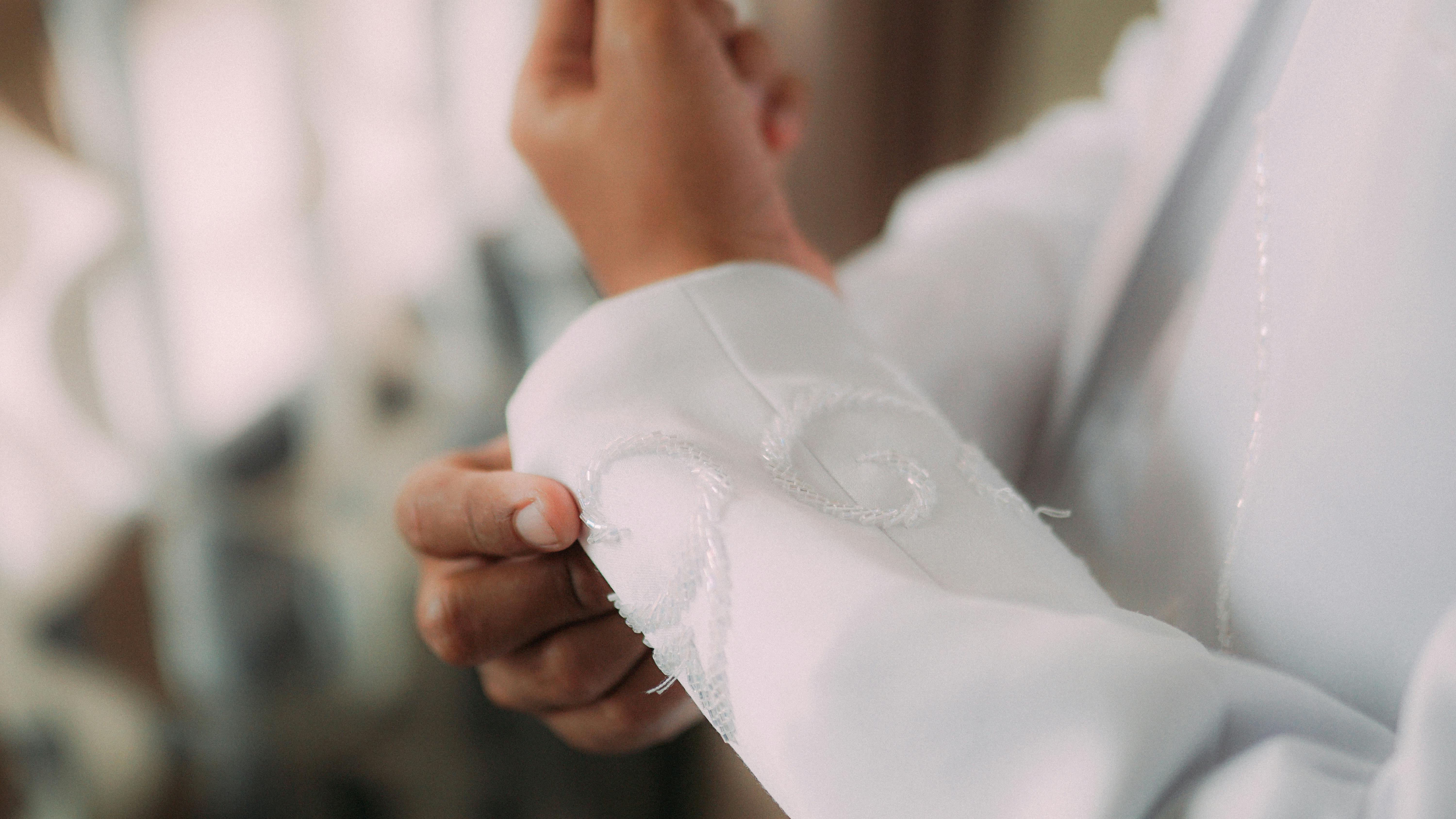 Hands adjust the cuff of a white jacket in a sewing workshop