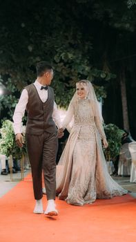 A bride and groom walking joyfully on a red carpet during their beautiful outdoor wedding ceremony.