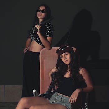 Two young women pose confidently with props, creating a striking indoor scene.