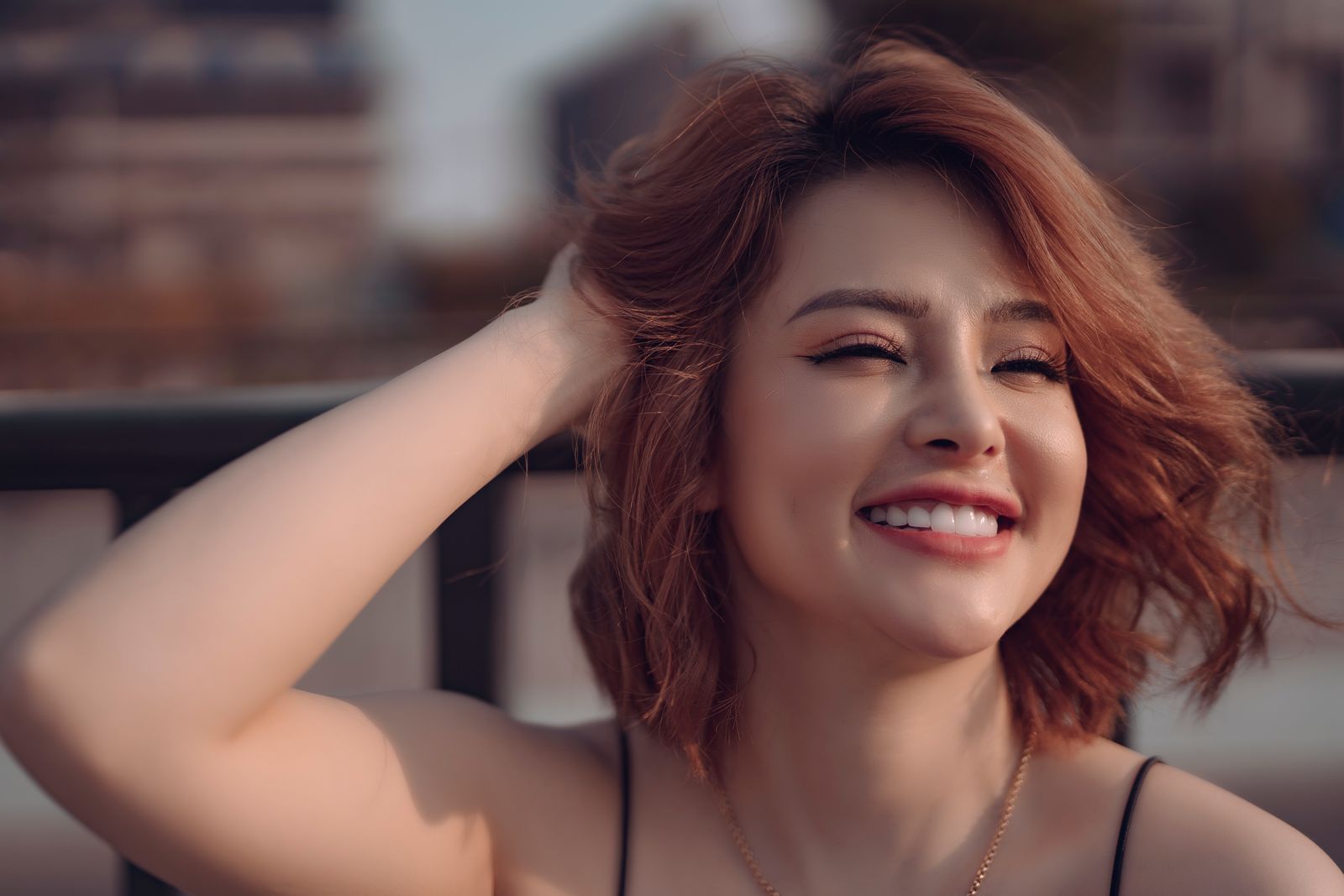 Woman with auburn hair smiling in warm sunlight while gently running her hand through her hair