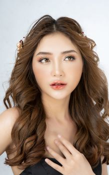 Young ethnic female in makeup and black wear with wavy hairdo and head accessories looking away on white background in studio