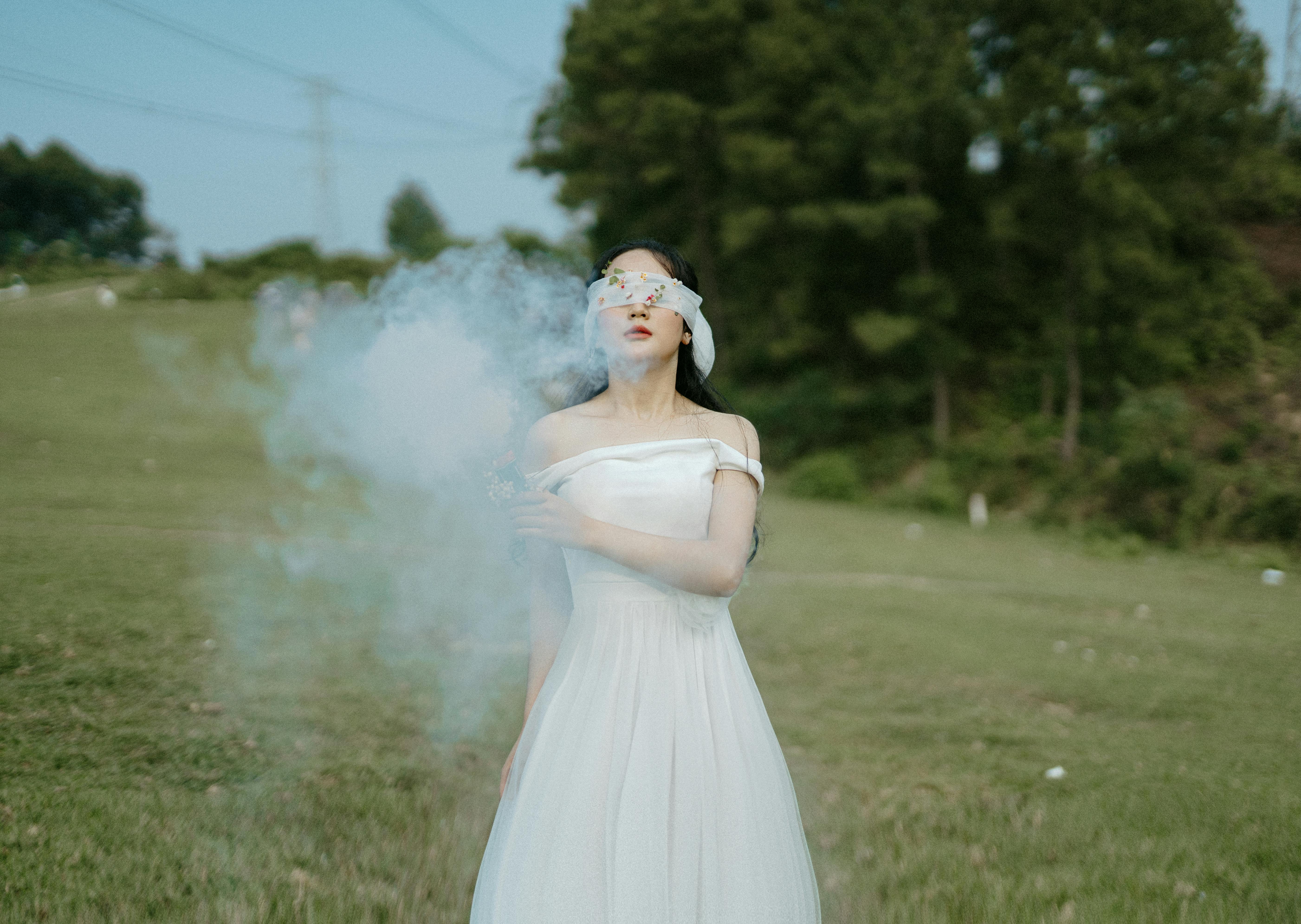 unrecognizable female in wedding dress in white smoke on field