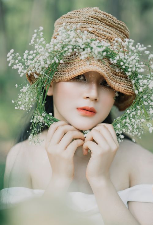 Free Emotionless ethnic woman wearing hat and white dress with floral wreath in summer countryside looking at camera Stock Photo