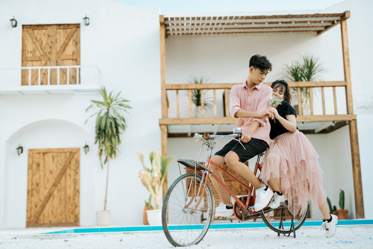 Asian Couple In Street Near Cottage On Bike