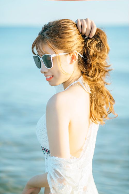 Free Side view of smiling female tourist in sunglasses adjusting hair standing on seashore Stock Photo