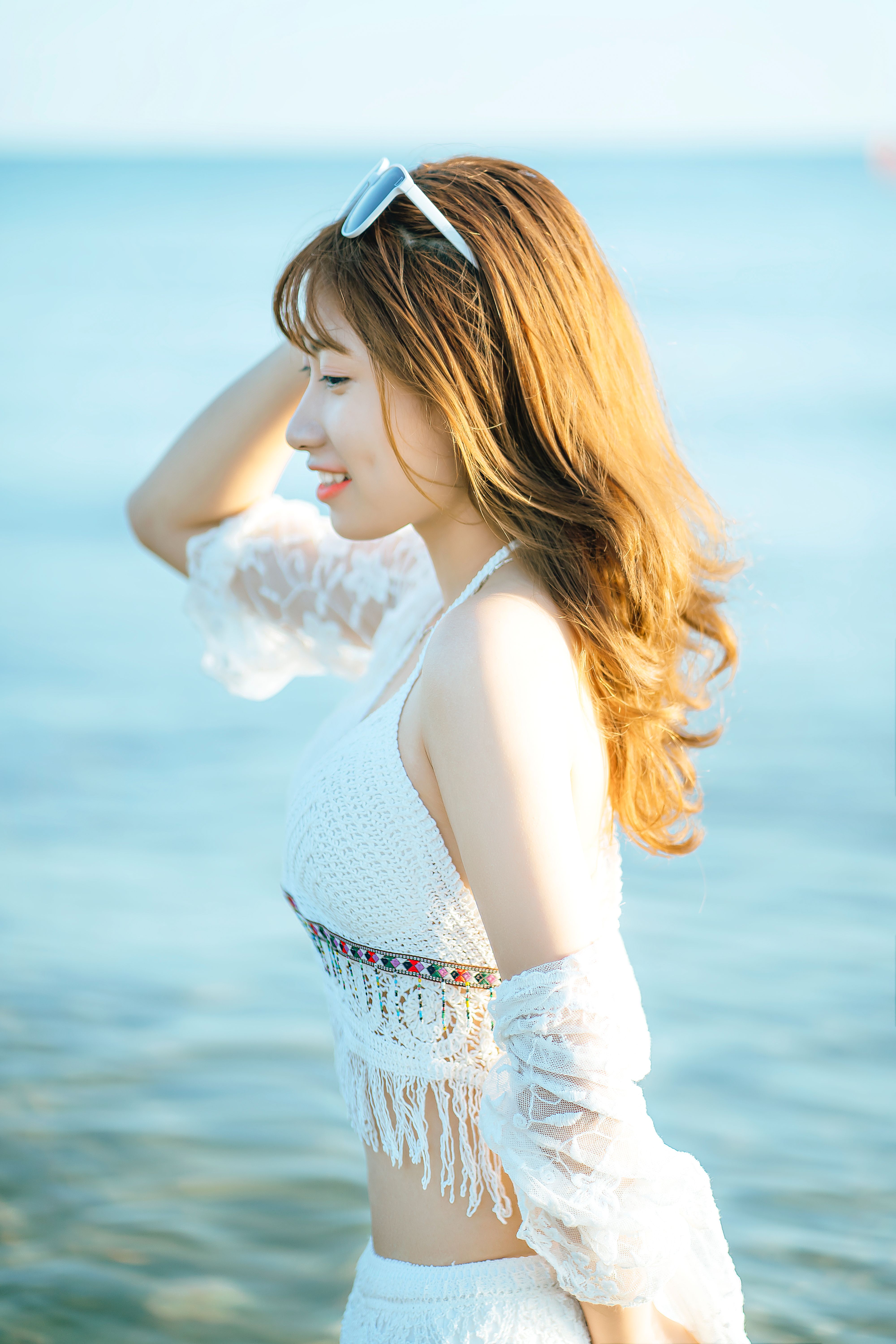 Side view of smiling ethnic female traveler wearing white beachwear standing in seawater during trip