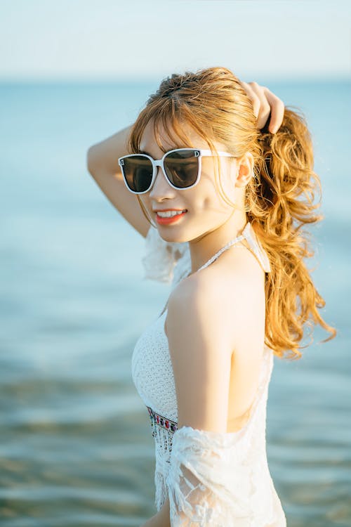 Free Cheerful Asian woman in modern sunglasses against ocean Stock Photo