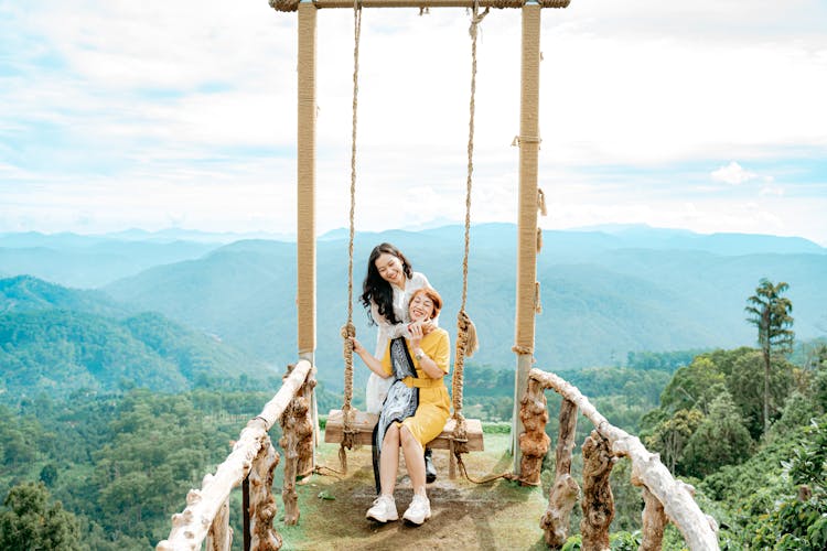 Content Asian Mom With Daughter On Swing Against Green Mounts