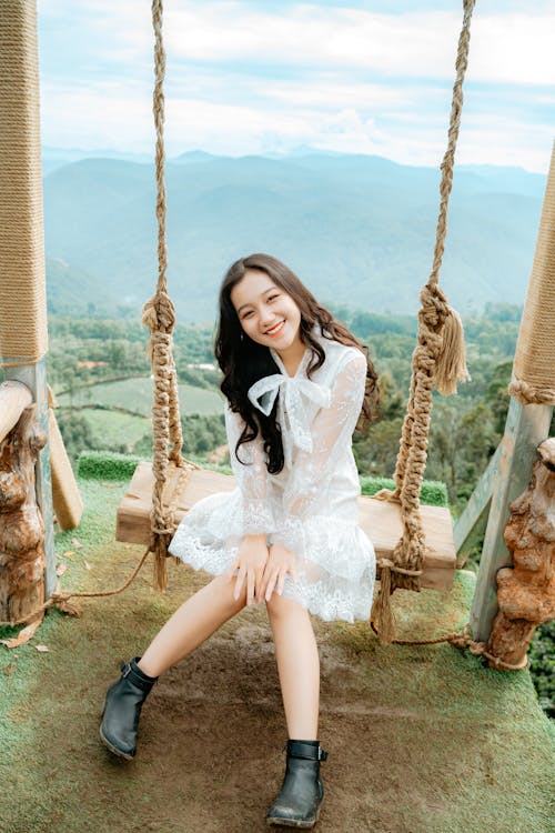 Cheerful ethnic woman on swing against mountain