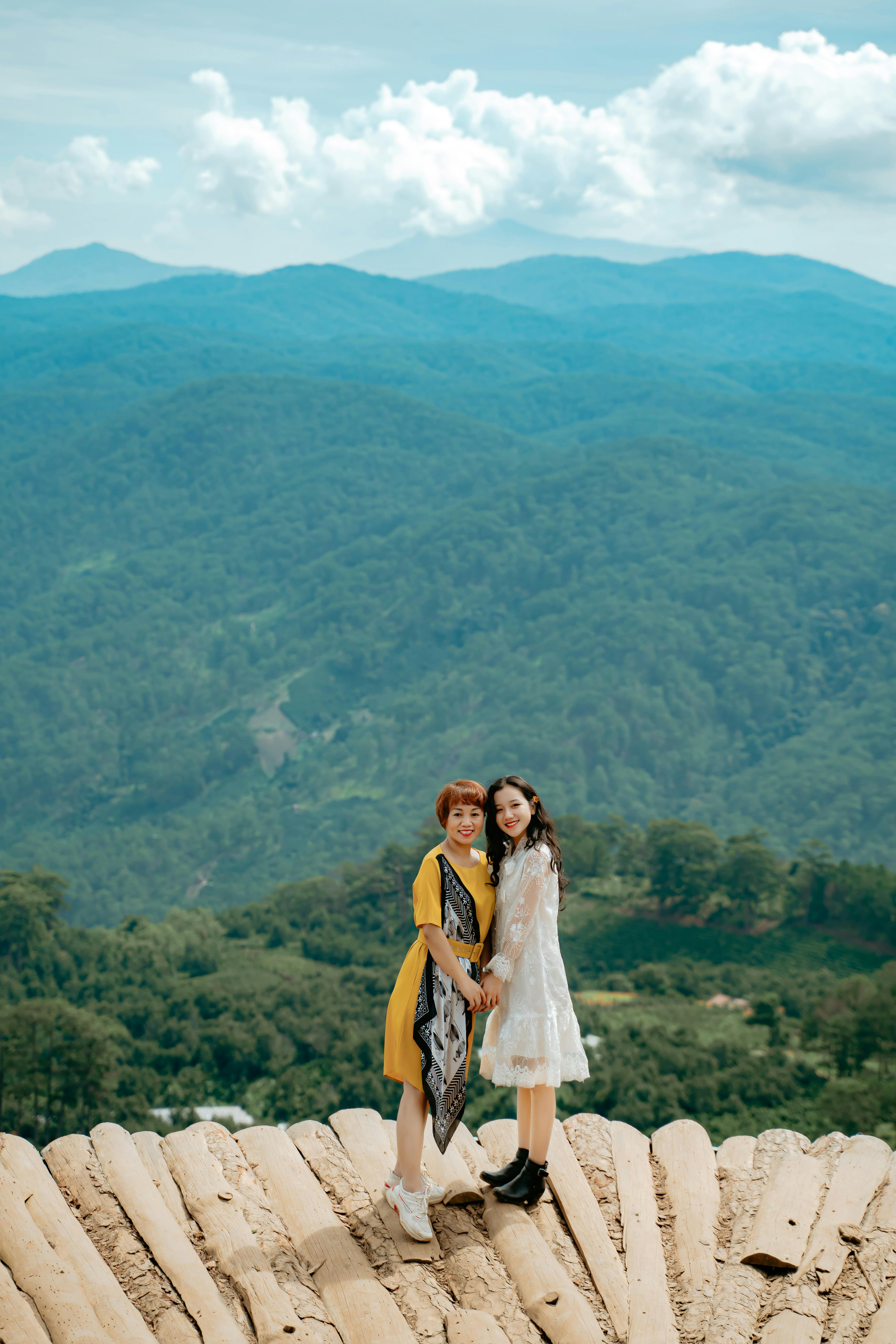 cheerful young ethnic ladies holding hands and resting on viewpoint in mountainous valley