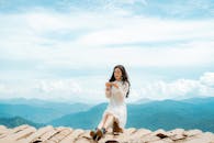 Stylish young Asian female tourist resting on roof in mountainous countryside