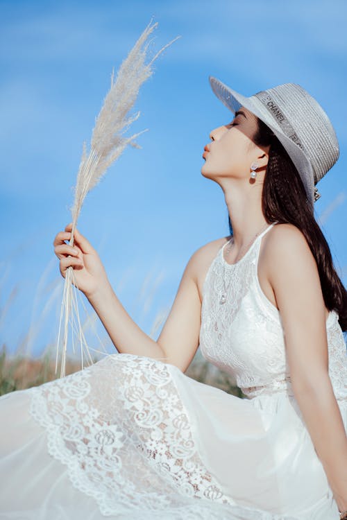 白い日よけ帽をかぶった白い花のスパゲッティストラップドレスの女性