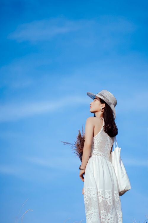Free Back view of young slender female in white dress and straw hat taking sunbath while spending holidays in nature Stock Photo
