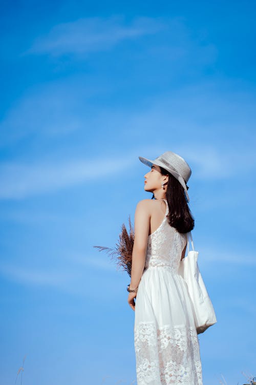 白色無袖連衣裙穿著白色太陽帽站在藍藍的天空下的女人