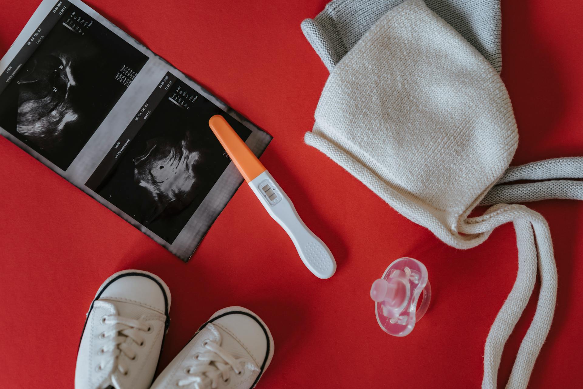 Close-Up Shot of Pregnancy Test and Ultrasound Result Near Baby's Things